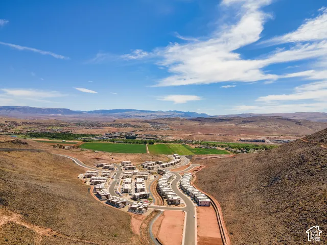 Aerial perspective showcasing multi-unit residential structures situated within a high-desert landscape, featuring paved access roads, proximity to open agricultural expanses, and an expansive mountain range backdrop
