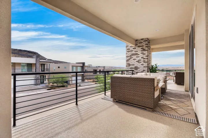 Covered balcony featuring a decorative brick pillar, horizontal metal railing, and neutral-toned flooring