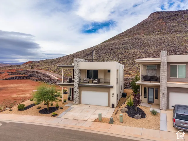 Modern multi-level exterior featuring stone facade accents, second-story balconies with cable railings, and a concrete driveway set against a mountain backdrop