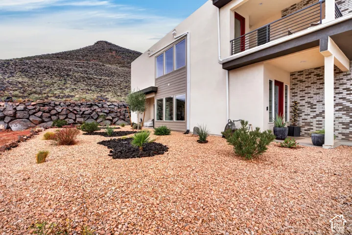 Contemporary exterior featuring stucco and brick masonry, large multi-pane windows, a second-story balcony with metal railings, and xeriscaped grounds with a decorative rock retaining wall