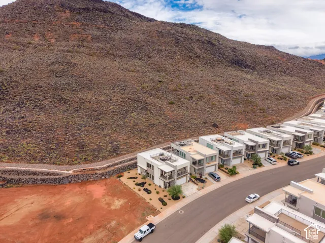 Modern multi-level exterior featuring clean geometric lines, stacked stone accents, integrated rooftop terraces, and desert-inspired landscaping against a prominent rock hillside backdrop