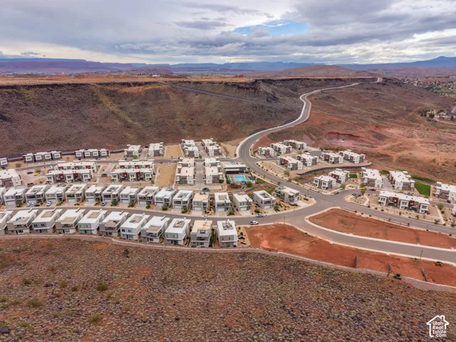 Aerial perspective of a multi-unit residential community featuring desert landscape, paved roadways, and a central swimming pool