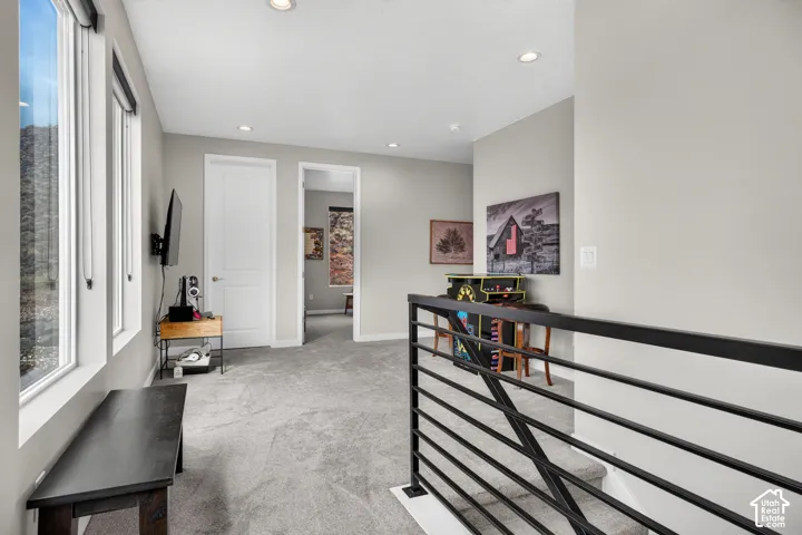 Neutral-toned interior space featuring recessed lighting, carpeted flooring, large windows, and a matte black metal stair railing