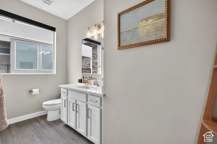 Bathroom featuring a vanity with white cabinetry, a solid-surface countertop with an integrated basin, wood-finish flooring, a wall-mounted light fixture with glass shades, and a large window