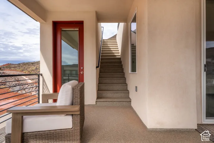 Covered patio featuring concrete-texture flooring, a red-frame glass door, cable railing, and exterior staircase
