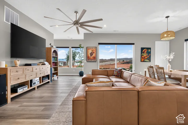Open-concept space featuring wood-finish flooring, a multi-blade ceiling fan, large windows, and a prominent pendant light fixture