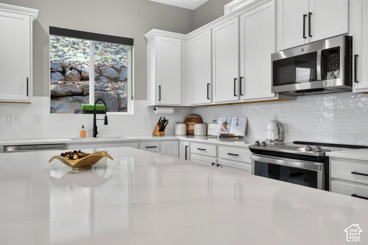 Kitchen featuring white shaker-style cabinetry, a large central island with white stone-finish countertop, subway tile backsplash, matte black hardware, and stainless steel appliances