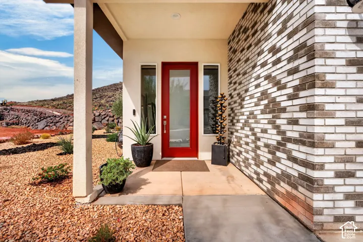 Covered entryway featuring a red glass-panel door, vertical side windows, two-tone brick facade, and recessed ceiling lighting