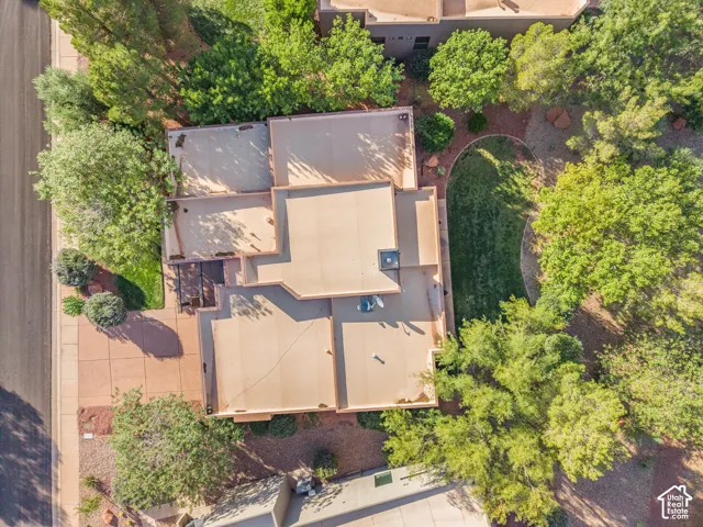 Aerial view showcasing a substantial patio with geometric pavers and defined sections, surrounded by mature landscaping and established trees providing natural privacy and shade throughout the grounds
