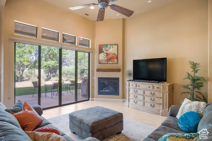 Vaulted ceiling with a ceiling fan, gas fireplace with a wood mantel, tile flooring, and a sliding glass door to the exterior patio