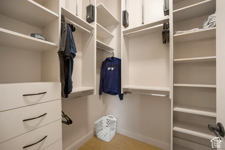 Spacious walk-in closet featuring custom built-in cabinetry with three deep drawers, extensive shelving throughout, multiple hanging rods, and warm wood-finish flooring