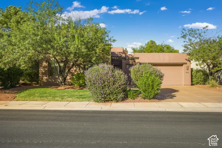 Stucco exterior, attached garage, concrete driveway, mature landscaping, and established lawn