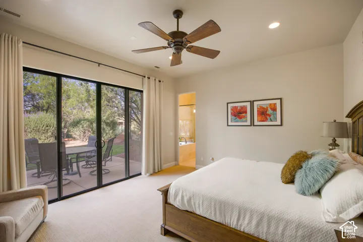 Master bedroom with sliding glass doors opening to a private patio, ceiling fan with dark finish, neutral carpeting, and framed artwork accents