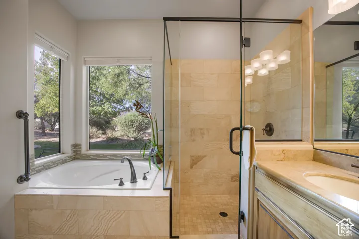 Soaking tub with bronze fixtures, glass-enclosed shower with tile surround, and a vanity with an integrated sink and mirror