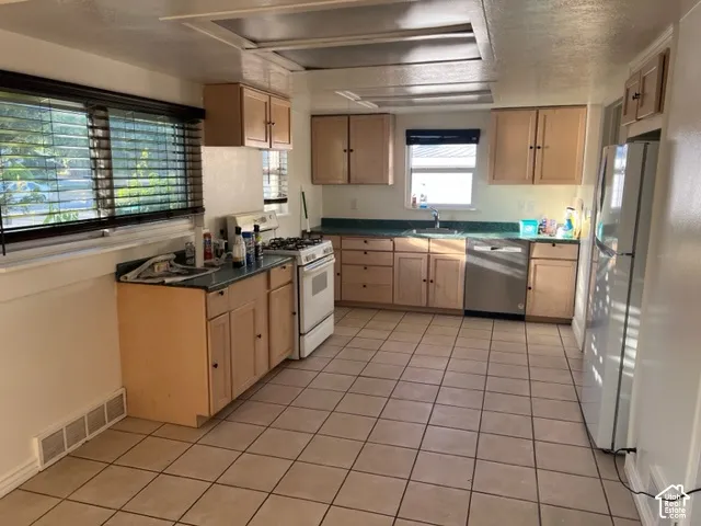 Kitchen featuring light-finish cabinetry, ceramic tile flooring, solid-surface countertops, and a stainless steel dishwasher