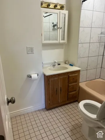 Bathroom featuring a wood-finish vanity with a composite countertop, wall-mounted medicine cabinet, four-light vanity fixture, and tiled tub surround