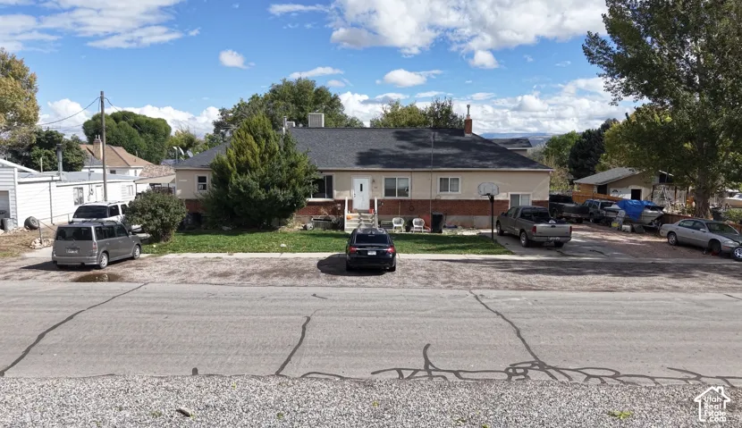 Single-story residence featuring a mixed brick and stucco exterior, shingled roof, mature landscaping, and an expansive paved off-street parking area