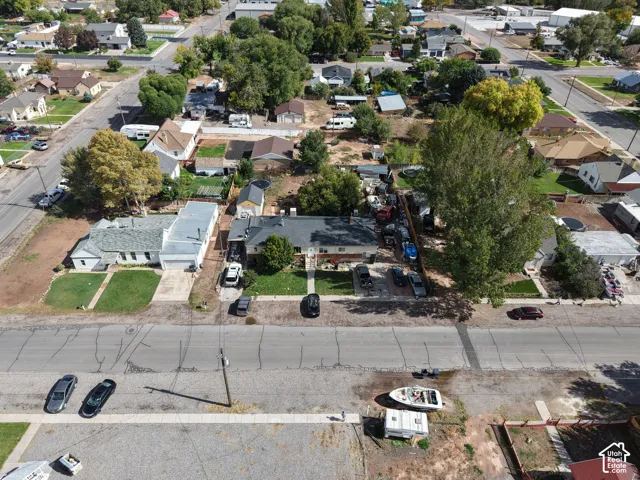 Aerial perspective featuring a mid-sized lot with a single-story structure, asphalt roofing, mature trees, and a concrete walkway