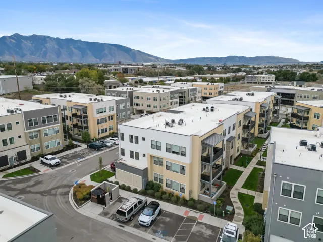 Multi-level residential complex featuring stucco and stone facade, private balconies, paved surface parking, and a backdrop of mountain scenery