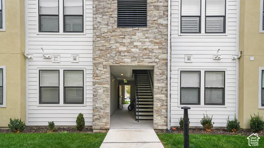 Exterior facade featuring horizontal siding, natural stone veneer, multiple windows with dark frames, and a concrete walkway
