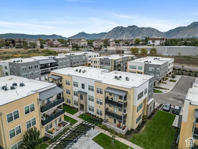 Multi-story residential complex featuring stucco and stone facade, private balconies with metal railings, flat roofing systems, and landscaped grounds with a metal pergola
