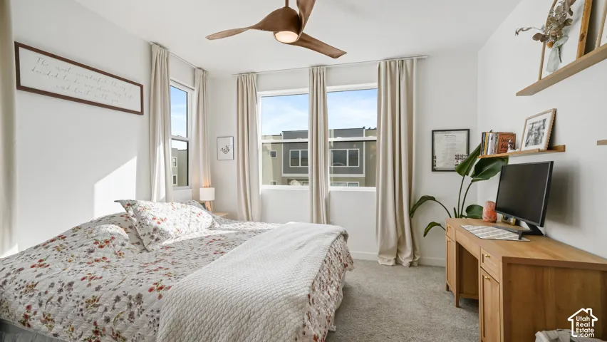 Bedroom featuring wall-to-wall carpeting, oversized windows with window treatments, and a central ceiling fan with integrated lighting