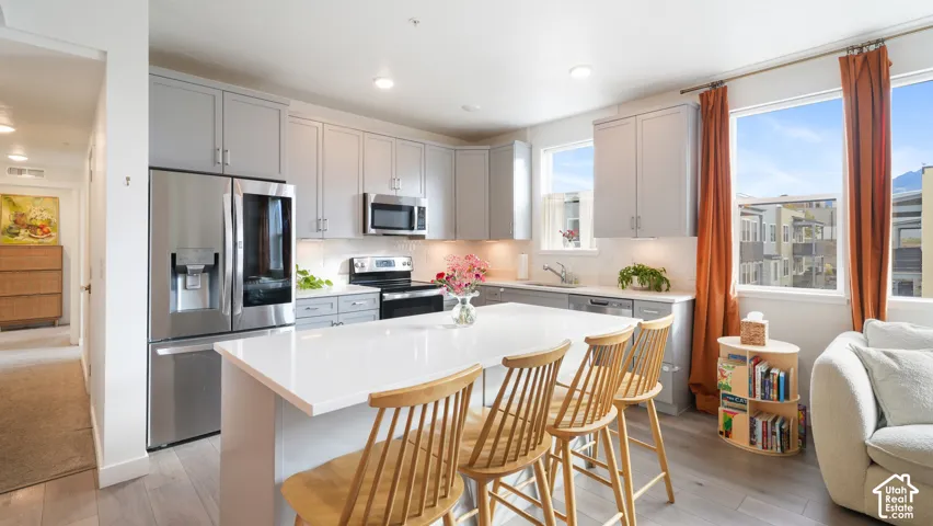 Kitchen featuring grey shaker-style cabinetry, quartz countertops, a central island, stainless steel appliances, and wood-finish flooring