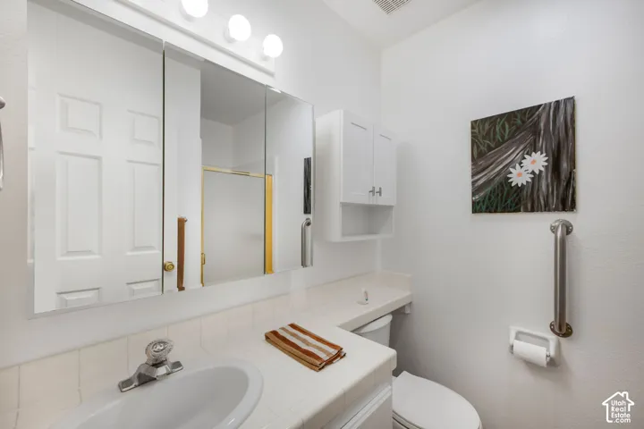 Bathroom vanity with integrated tile countertop, tri-fold mirrored medicine cabinet, four-light vanity fixture, white wall-mounted cabinetry, and a chrome grab bar