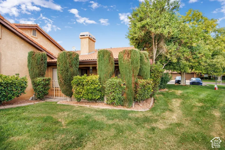 Stucco exterior featuring a clay tile roof, a masonry chimney, and landscaped grounds with mature trees and shaped shrubbery