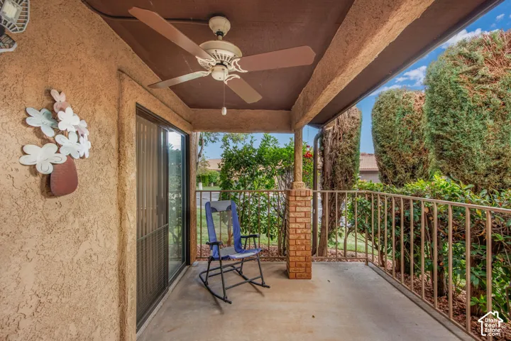Covered patio featuring a concrete floor, ceiling fan, stucco wall finish, and a brick-based metal railing
