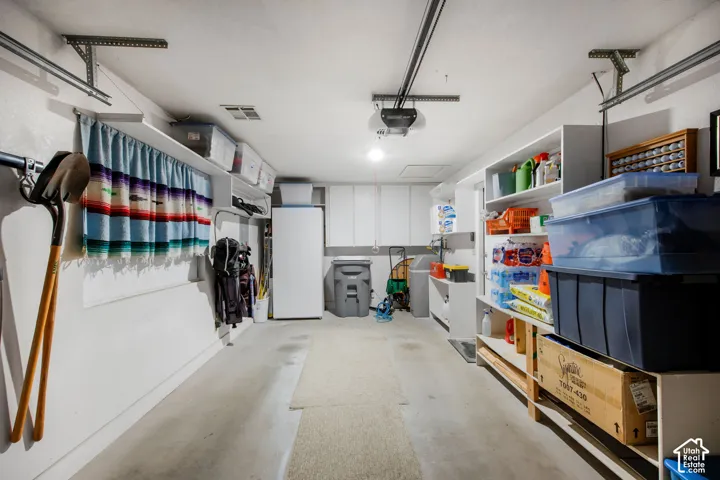 Two-car garage featuring white built-in wall cabinetry, extensive open shelving, and a ceiling-mounted automatic garage door opener
