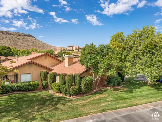 Stucco exterior with a tiled roof, exterior chimney, mature landscaping, and mountain backdrop