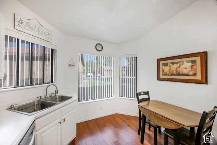 Corner space featuring wood-finish flooring, white cabinetry, a dual-basin stainless steel sink with a goose-neck faucet, and multiple windows with vertical blinds