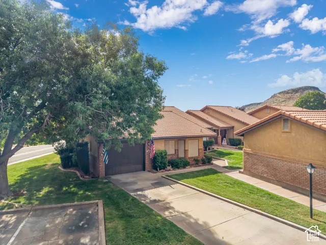 Single-story residence featuring a tile roof, brick and stucco exterior, attached garage, and paved driveway, set against a mountain backdrop