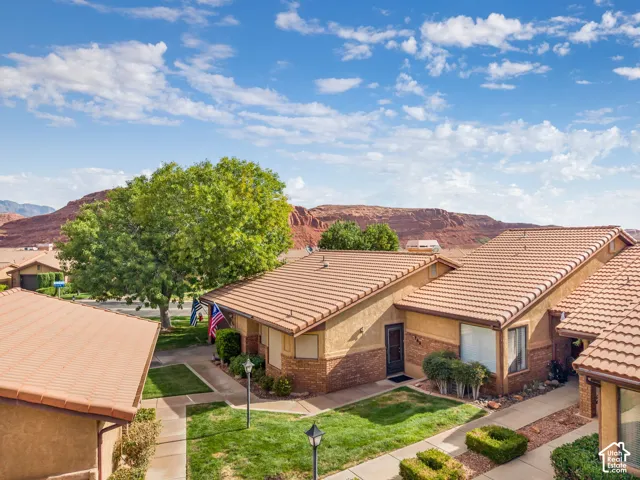 Exterior facade featuring stucco and brick siding, terra cotta tile roofing, and integrated walkways, set against a backdrop of red rock mountainous terrain