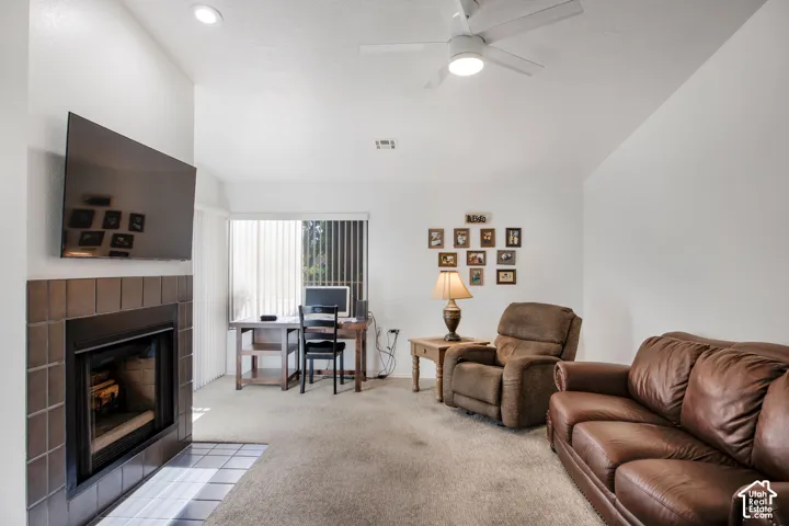 Living area featuring a fireplace with a square tile surround, vaulted ceilings, a ceiling fan, and vertical window blinds