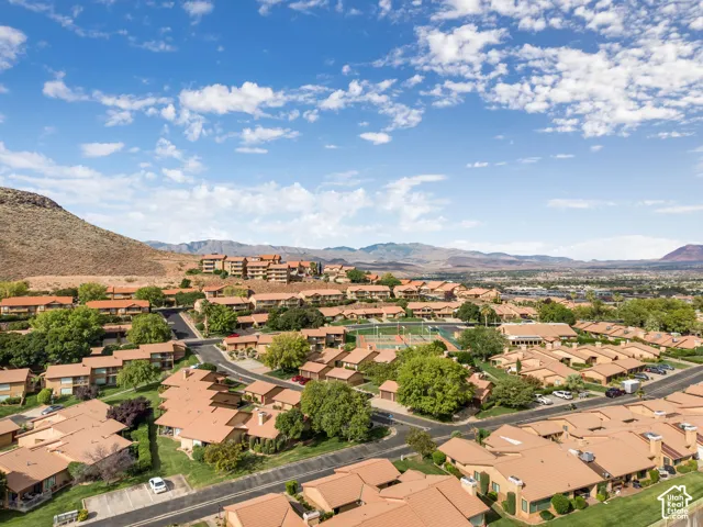 Aerial perspective of a multi-unit residential community featuring red-tile roofing, established landscaping, tennis courts, and a prominent mountain backdrop
