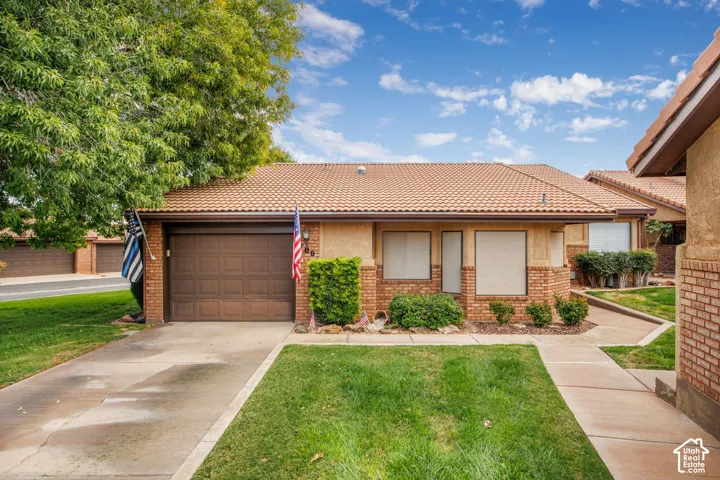 Single-level exterior featuring a brick and stucco facade, concrete tile roof, attached one-car garage, and a concrete driveway