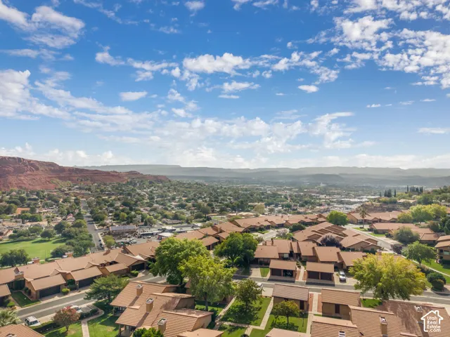 Aerial perspective featuring a residential community with red rock mountain backdrops, paved roads, and mature trees