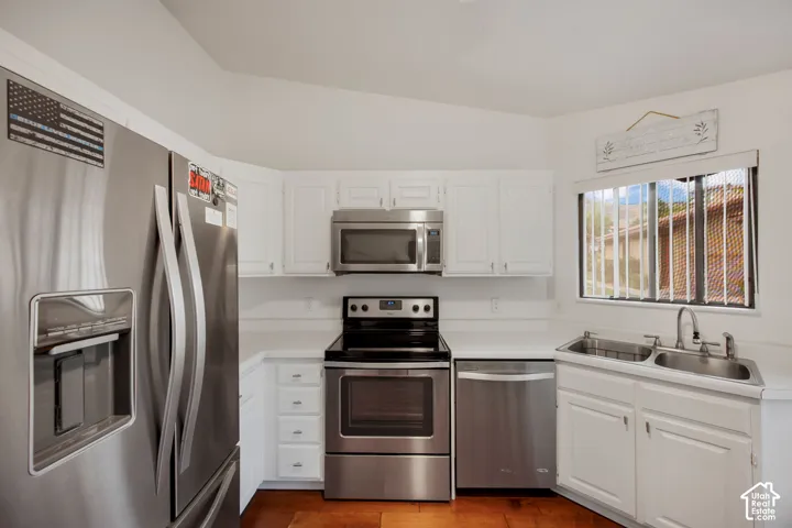 Kitchen featuring stainless steel appliances, white cabinetry, solid surface countertops, a dual-basin sink, and wood-finish flooring