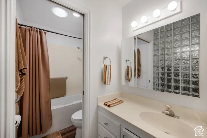 Bathroom featuring a vanity with an integrated sink and solid-surface countertop, a multi-bulb light fixture, a mirrored medicine cabinet, a glass block accent window, and a tub-shower combination