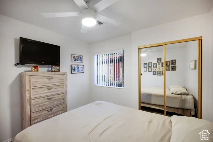 Room featuring a central ceiling fan with an integrated light fixture, a window with vertical blinds, and a built-in closet with mirrored sliding doors and gold-tone trim