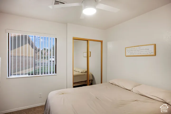 Room featuring neutral wall finishes, carpeted flooring, a ceiling fan with integrated lighting, a window with vertical blinds, and a closet with sliding mirrored doors