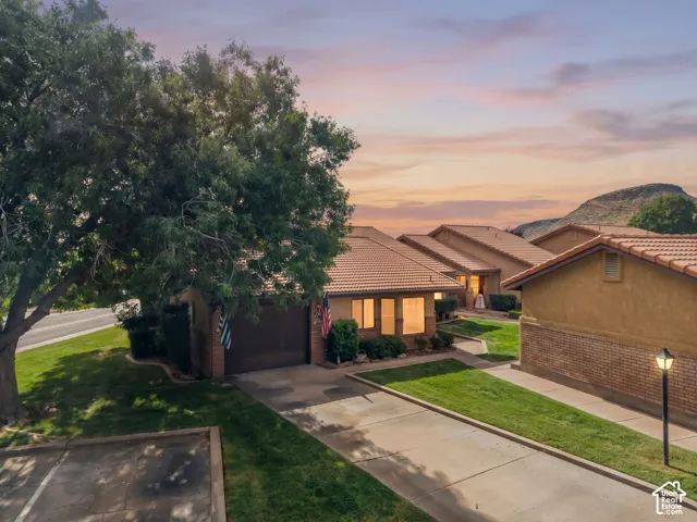 Stucco exterior with clay tile roofing, attached garage, concrete driveway, and established landscape