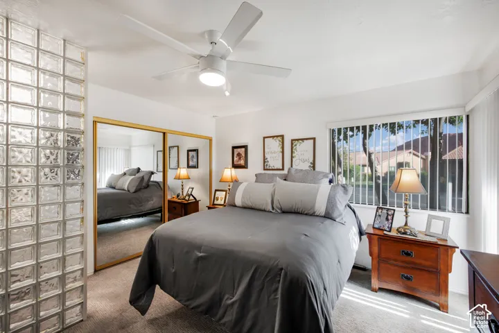 Glass block partition wall, sliding mirrored closet doors with gold-tone frames, neutral carpeting, and a white ceiling-mounted fan with integrated lighting