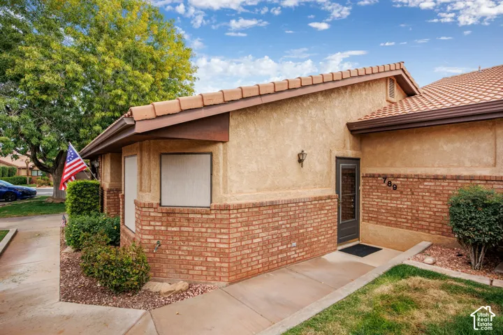 Stucco and brick facade with a tiled roof, exterior wall-mounted lighting, and a paved concrete walkway