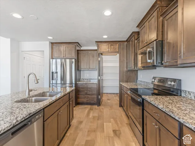 Kitchen featuring stained wood cabinetry, granite countertops, stainless steel appliances, wood-finish tile flooring, and a hidden walk-in pantry