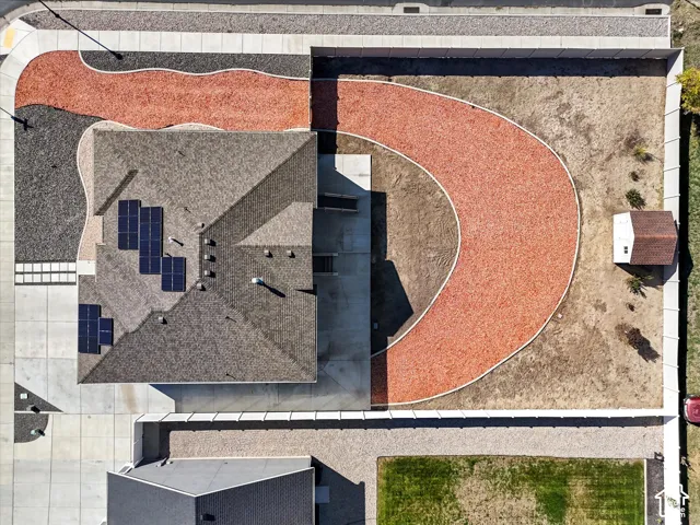 Aerial perspective featuring a residential lot with solar panels, detached storage shed, concrete driveway, and perimeter fencing