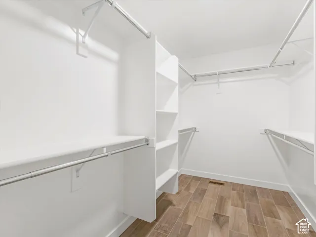 Primary bedroom walk-in closet featuring wood-finish tile flooring and white built-in shelving with integrated metal clothing rods