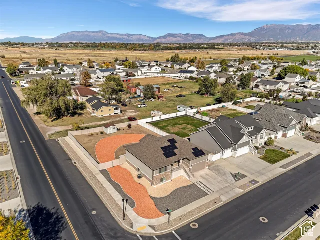 Corner lot residence featuring solar panel arrays, stone and siding exterior, privacy fencing, and zeroscaped front yard landscaping set against a mountain backdrop